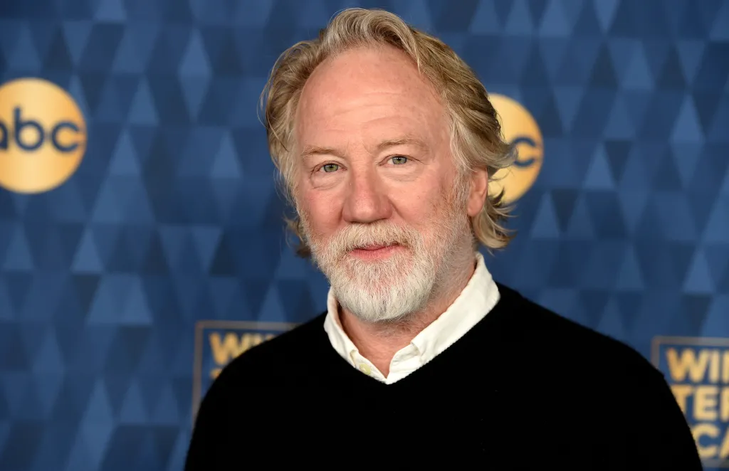Timothy Busfield with a white beard wearing a black sweater and white collared shirt.