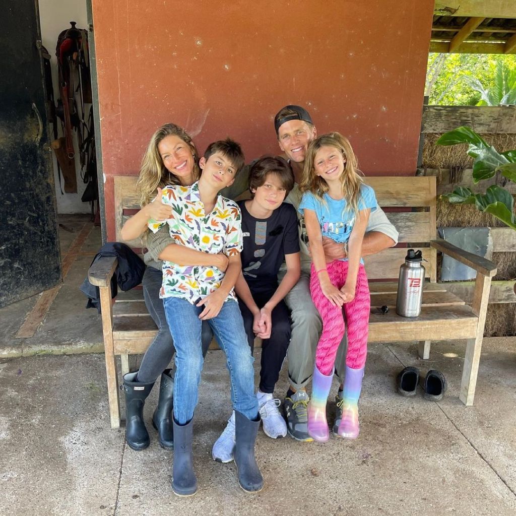 Gisele Bündchen and Tom Brady with their three children sitting together on a wooden bench.