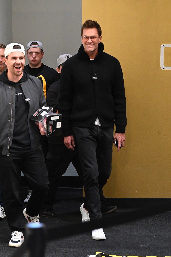Tom Brady with sunglasses and a black cardigan smiling, accompanied by other people, at the CardVault by Tom Brady Las Vegas Store.