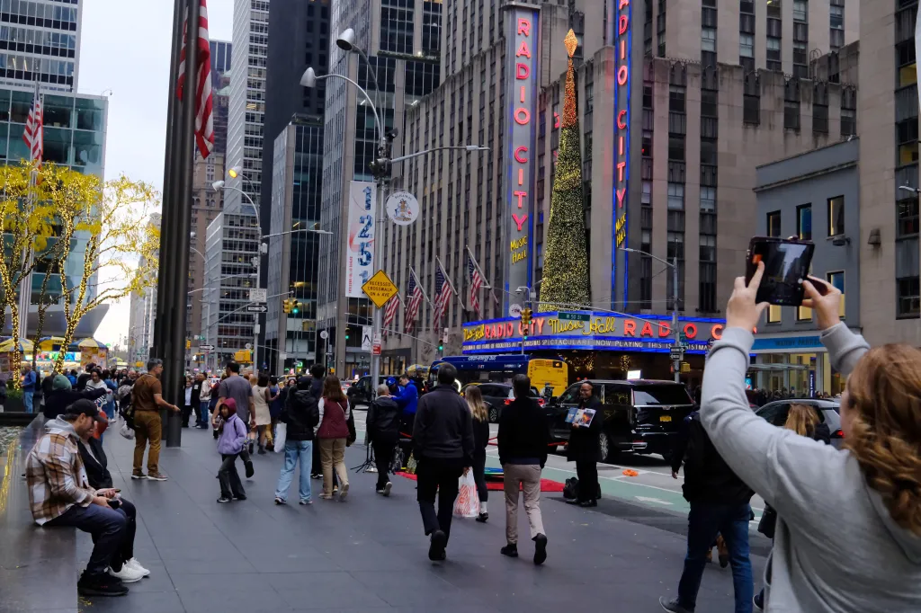 Crowds of tourists on a city sidewalk near Radio City Music Hall in New York.