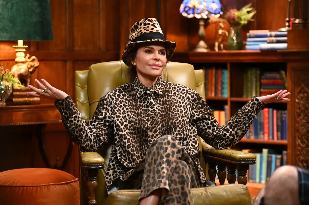 Lisa Rinna in a leopard print hat, shirt, and pants, sitting in a green leather armchair.