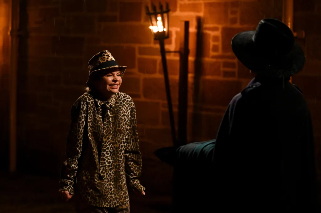 Lisa Rinna in a leopard print outfit and hat, speaking to another person in the dark.