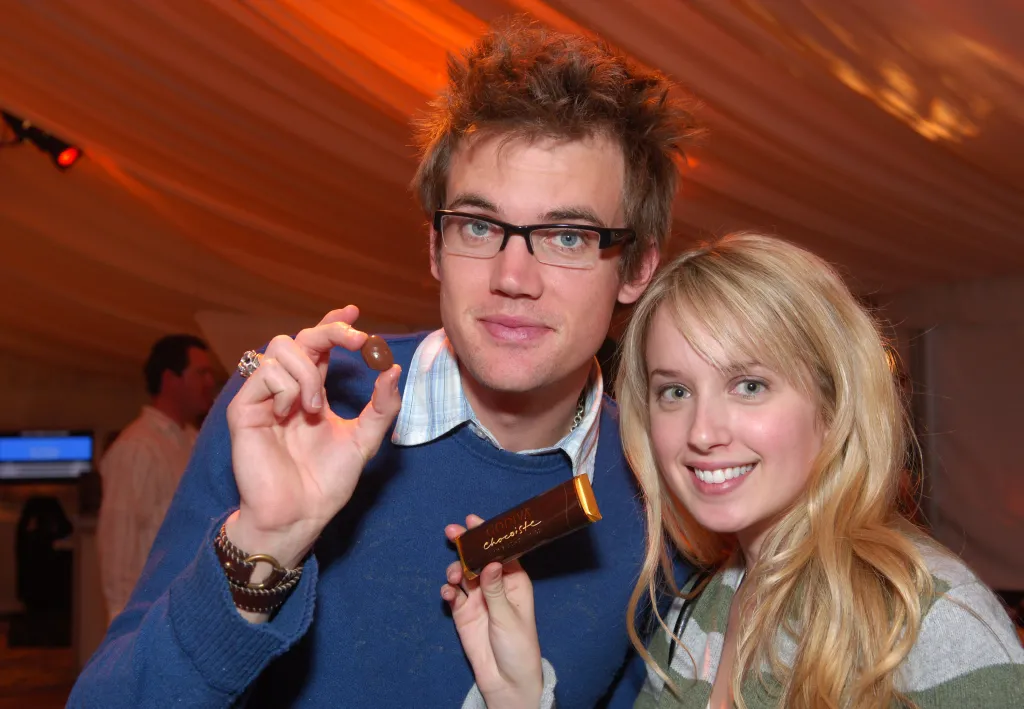Tyler Hilton and Megan Park smiling and holding Godiva chocolates.