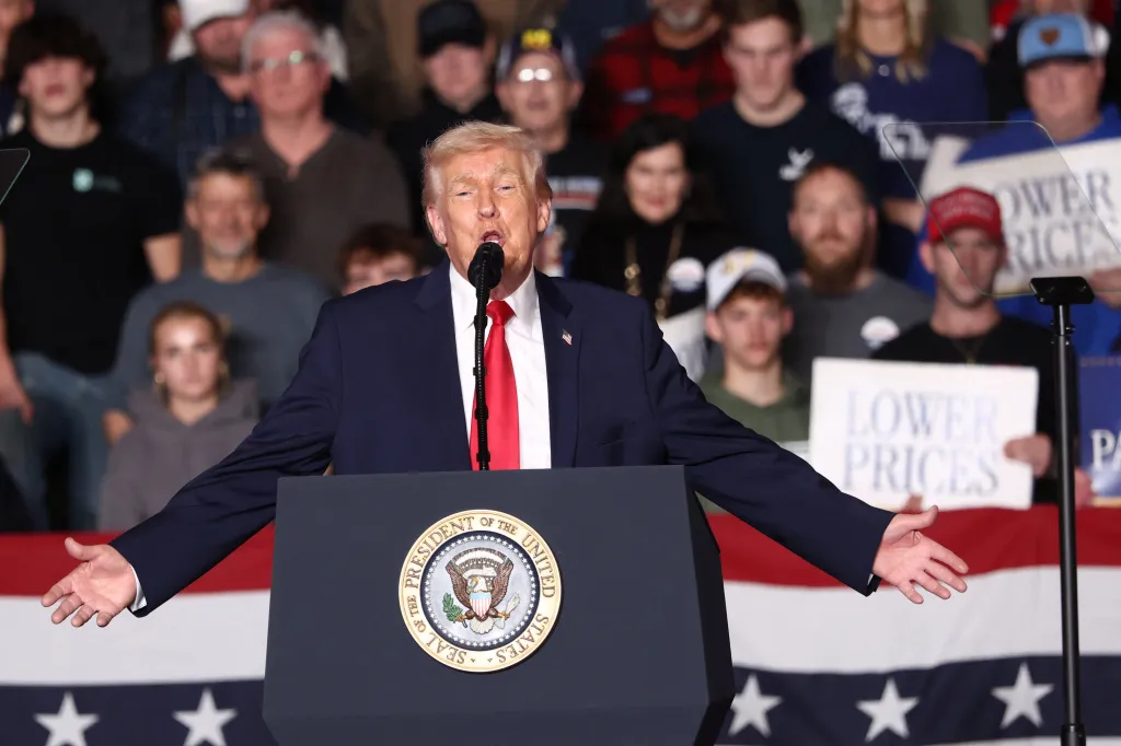 U.S. President Donald Trump speaking at a podium with outstretched arms to a crowd, with some holding signs that read 