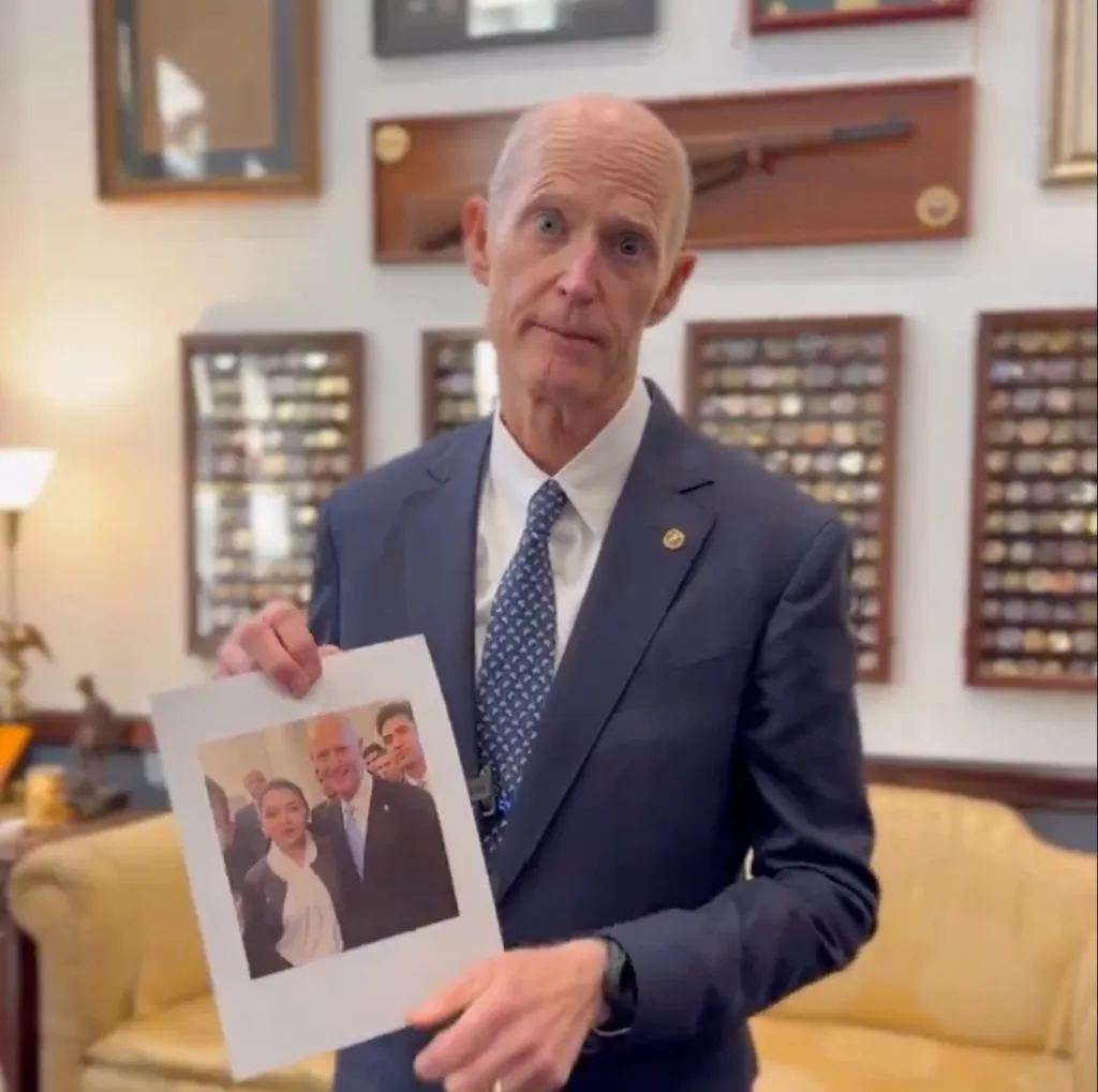 Senator Rick Scott holding up a photo of himself with Maria Oropeza.