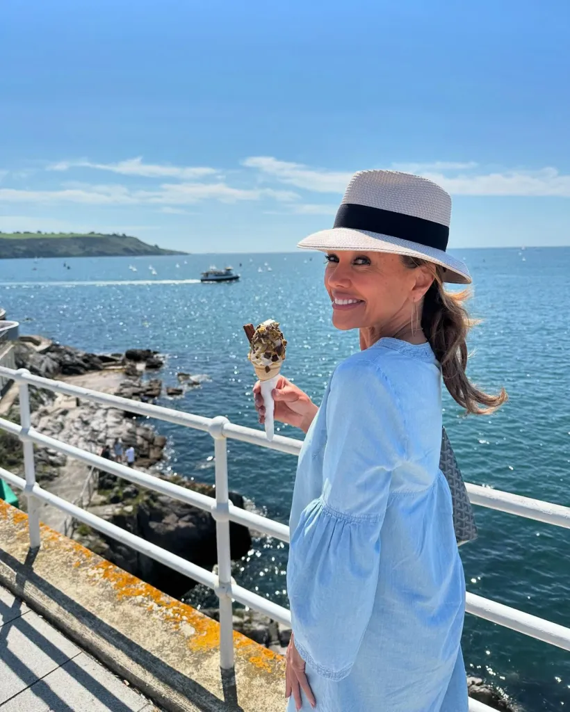 Vanessa Williams in a hat, holding an ice cream cone by the ocean.