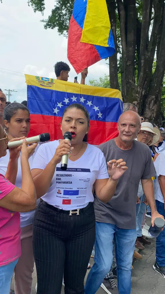 Venezuelan activist María Oropeza speaking into a microphone, with a Venezuelan flag behind her.