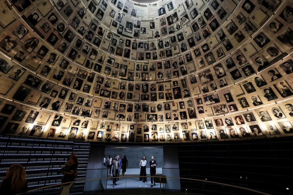 Visitors tour an exhibition featuring a domed wall covered in hundreds of black and white photos of Holocaust victims at Yad Vashem in Jerusalem.