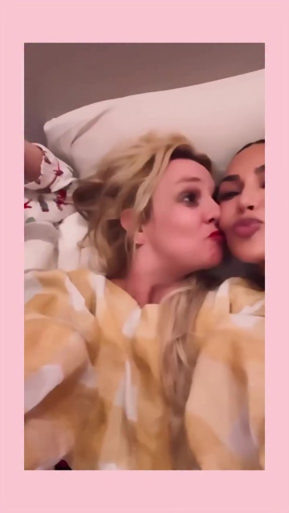 Britney Spears and Kim Kardashian laying down side-by-side, with Spears puckering her lips towards the other.