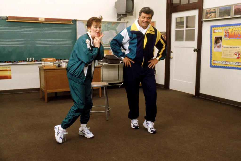 Catherine O'Hara and Fred Willard dancing in a classroom.