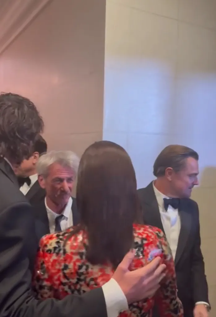 Jacob Elordi's mom, seen from behind with dark hair and a red, black, and white patterned dress, with Leonardo DiCaprio to her right and Sean Penn to her left, all in formal wear.