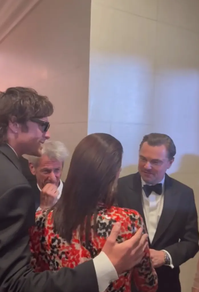 Jacob Elordi's mom, in a red and black floral dress, with her back to the camera, standing between Jacob Elordi and Leonardo DiCaprio.
