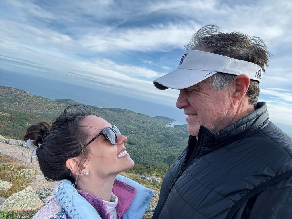 Jordon Hudson and Bill Belichick smiling at each other on a mountaintop.
