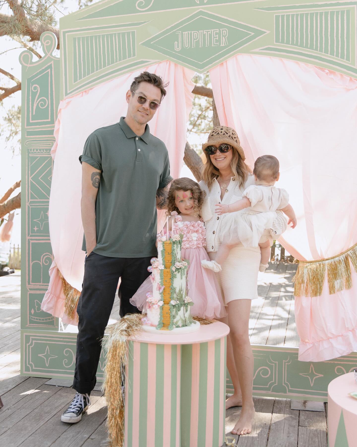 Ashley Tisdale, her husband Christopher French, and their two daughters pose in front of a circus-themed backdrop for a birthday celebration.