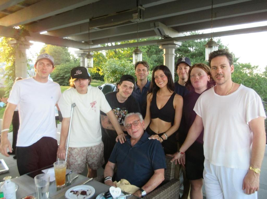 Nicola Peltz and her father Nelson with a large group of people on a patio.