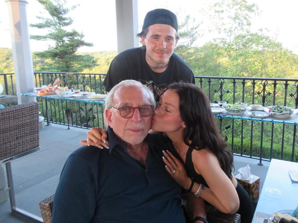 Nicola Peltz kissing her father Nelson Peltz on the cheek, with Brooklyn Beckham standing behind them.