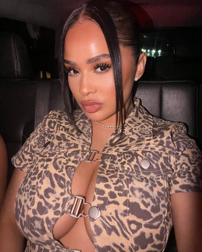 A woman in a leopard print top, from the waist up, sits in a dark vehicle.