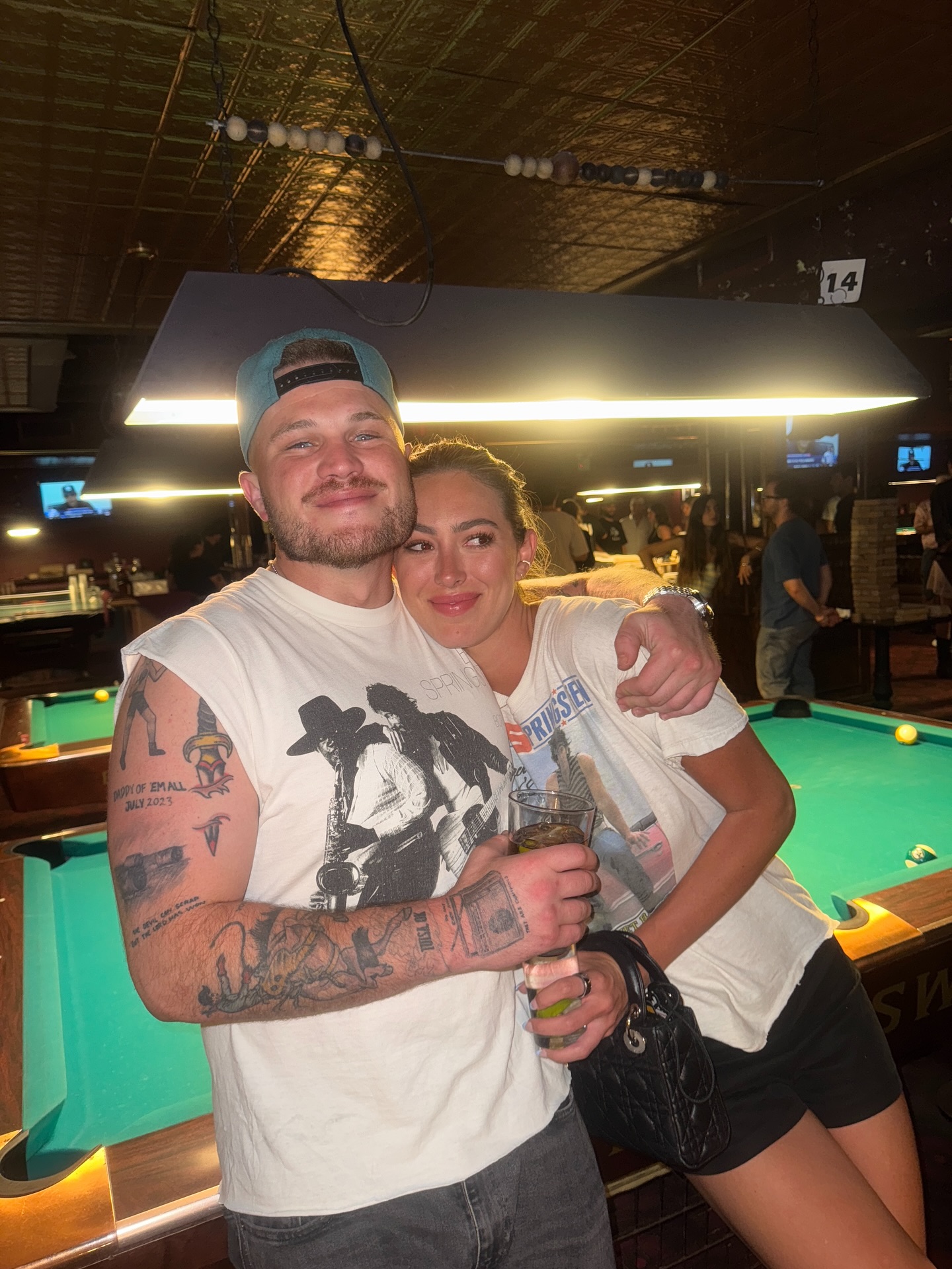 Zach Bryan and Samantha Leonard embracing while holding drinks.