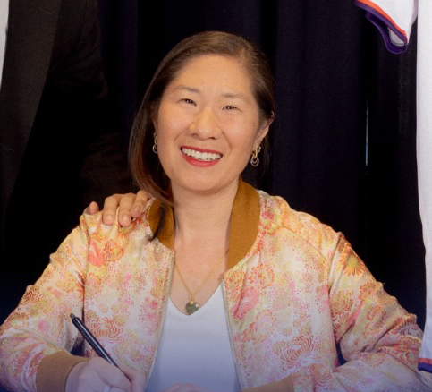 Louise Yeung, Chief Climate Officer, smiles while holding a pen over a document.