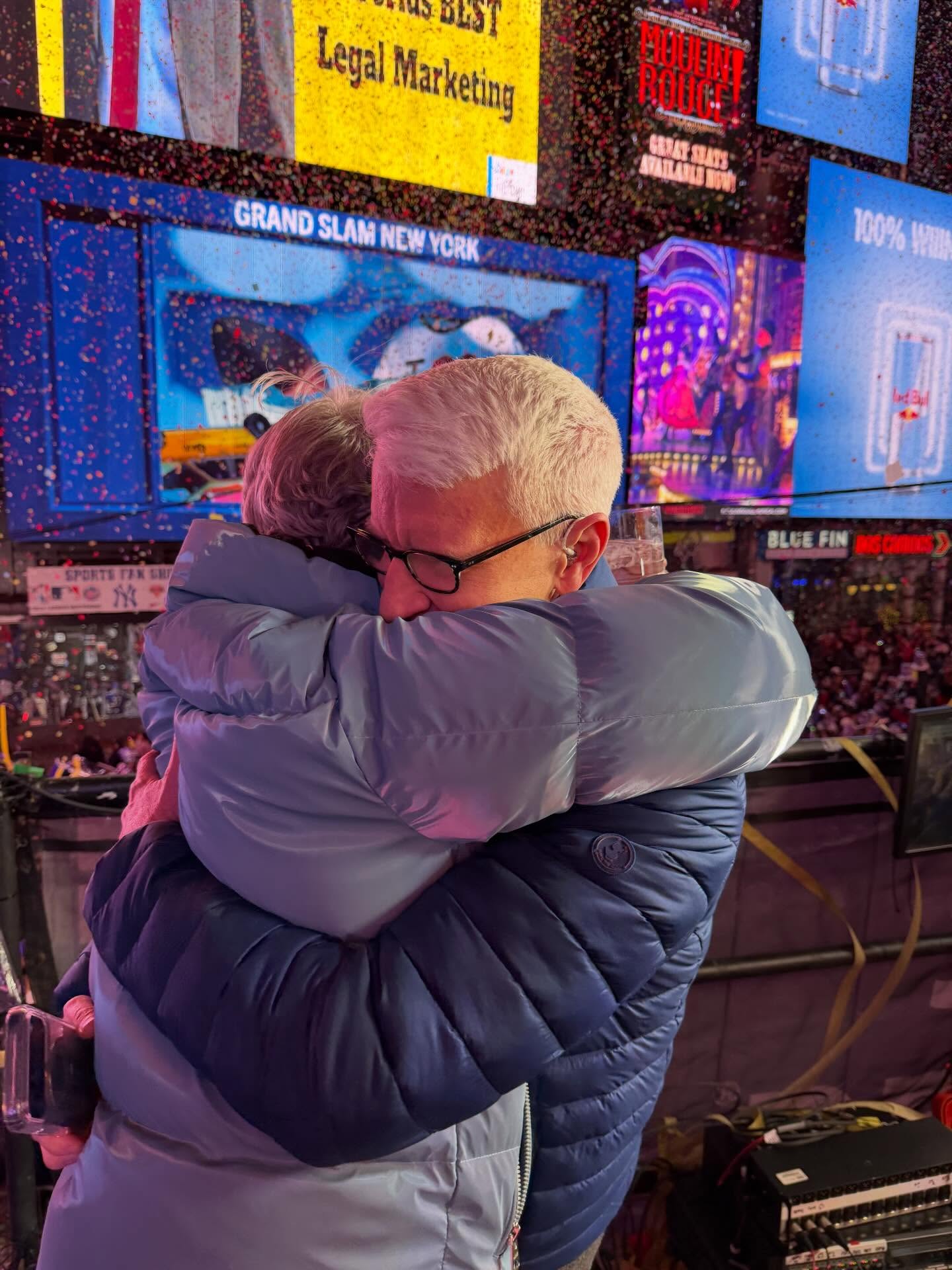 Anderson Cooper hugging Andy Cohen with confetti falling in Times Square.