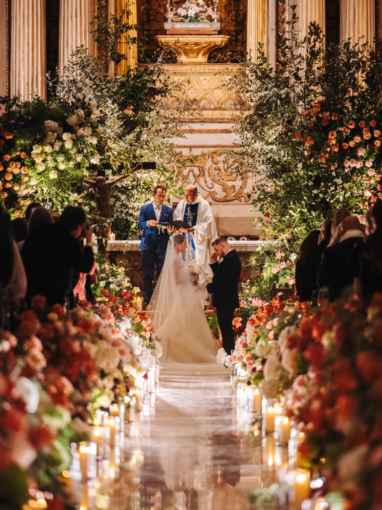 A bride and groom at the altar during their wedding ceremony, surrounded by flowers and candles.