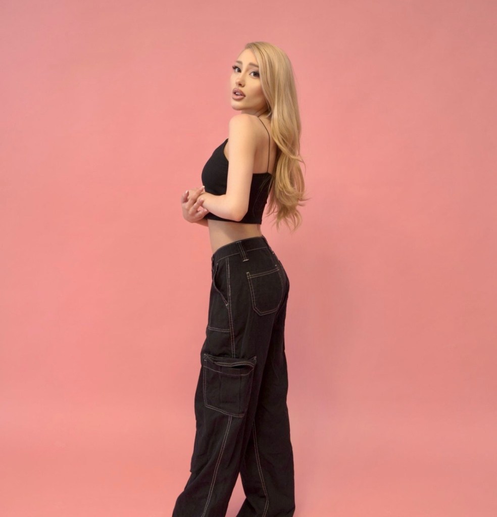 Paige Niemann, an Ariana Grande lookalike, posing against a pink background.