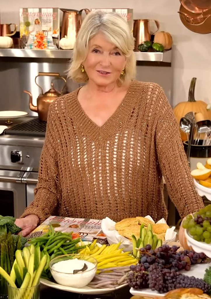 Martha Stewart stands in a kitchen with fresh produce and cookbooks.