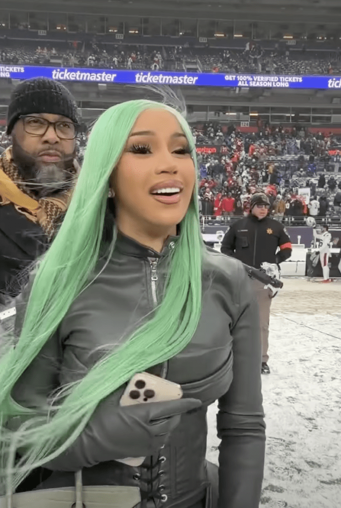 Cardi B with bright green hair at a stadium.