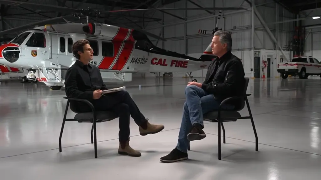 California Governor Gavin Newsom being interviewed by Jacob Soboroff of MS NOW in front of a CAL FIRE helicopter.