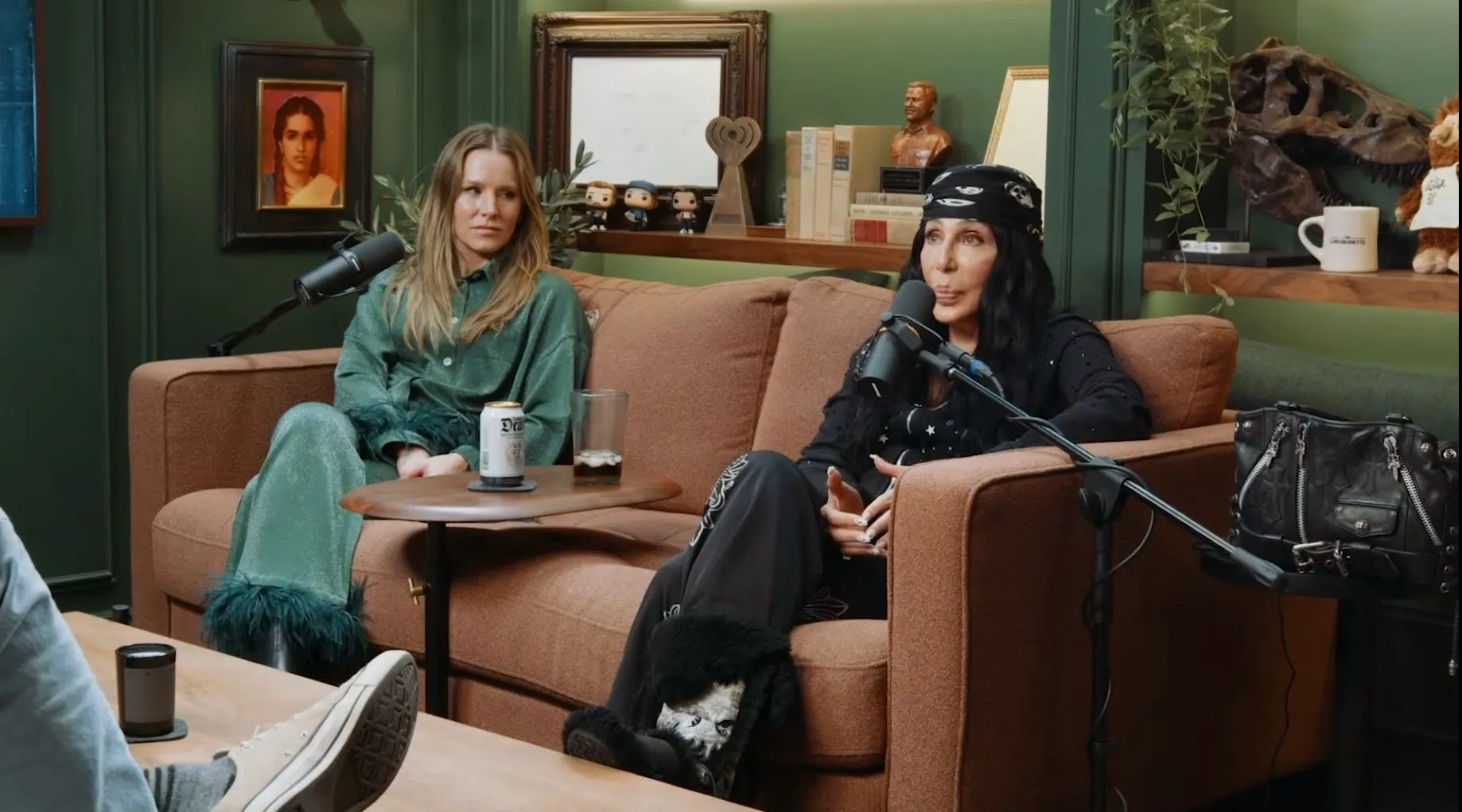 Kristen Bell and Cher sitting on a couch for a podcast interview.