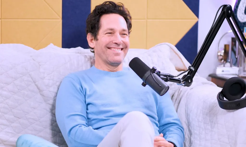 Paul Rudd smiling and sitting on a couch with a microphone in front of him.
