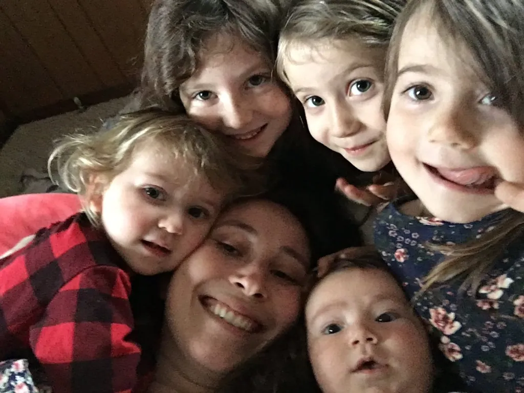 A woman and five children pose closely together for a selfie.
