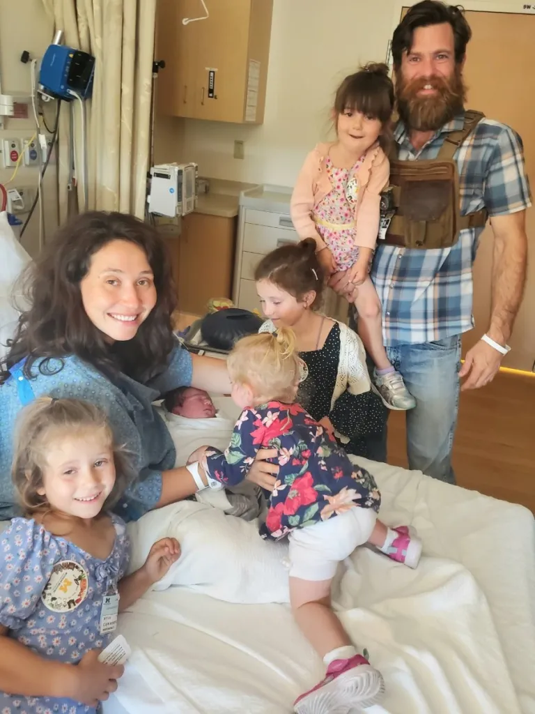 Family with four young girls and a newborn baby in a hospital room.