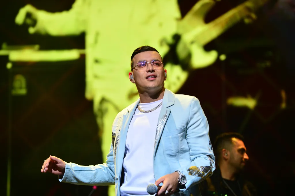 Yeison Jimenez performing live on stage in a light blue jacket and glasses.
