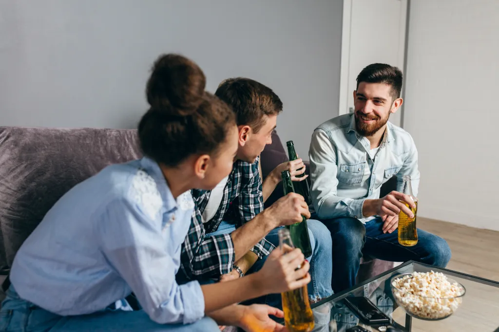 Three friends laughing and drinking beer at home.