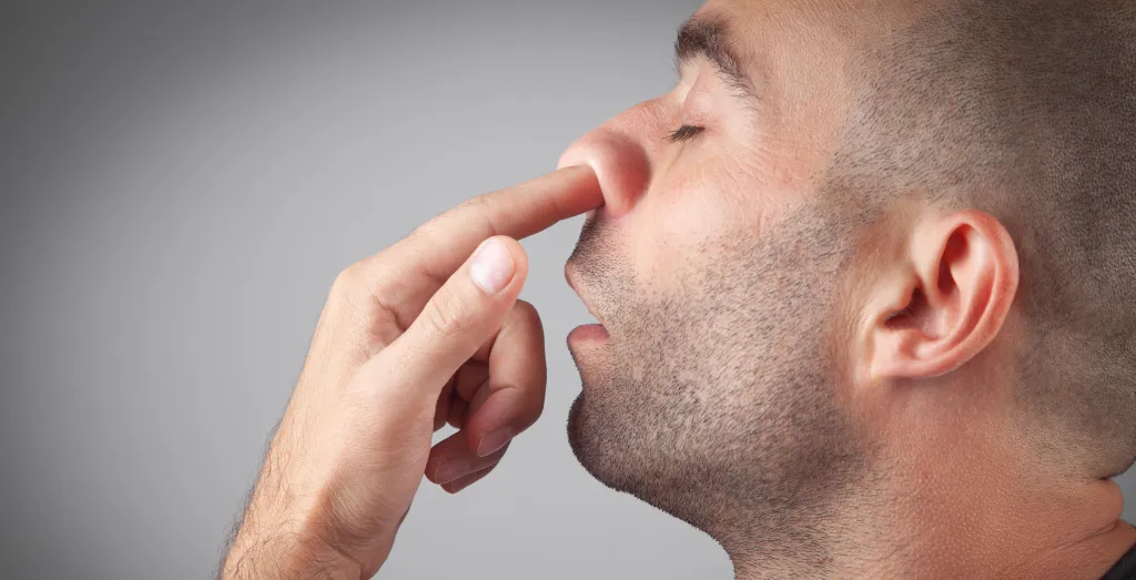 A young man with short hair and stubble picks his nose.