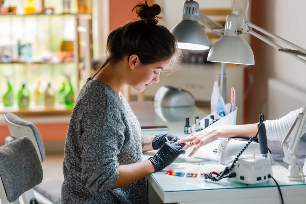 A young female manicurist wearing gloves performs a manicure on a client.