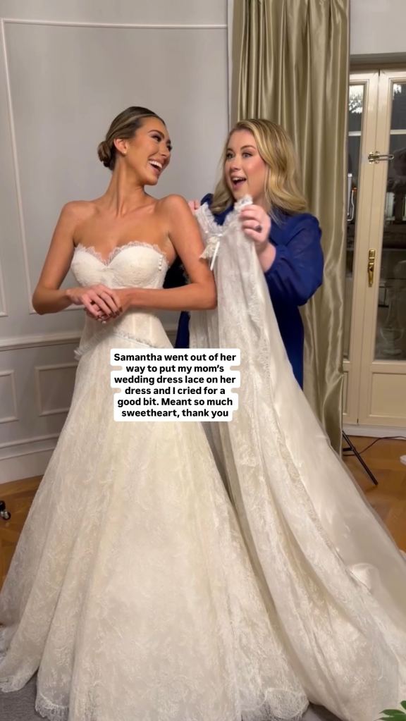 A woman in a strapless wedding dress smiles while another woman in a blue shirt helps her with the train of the dress.