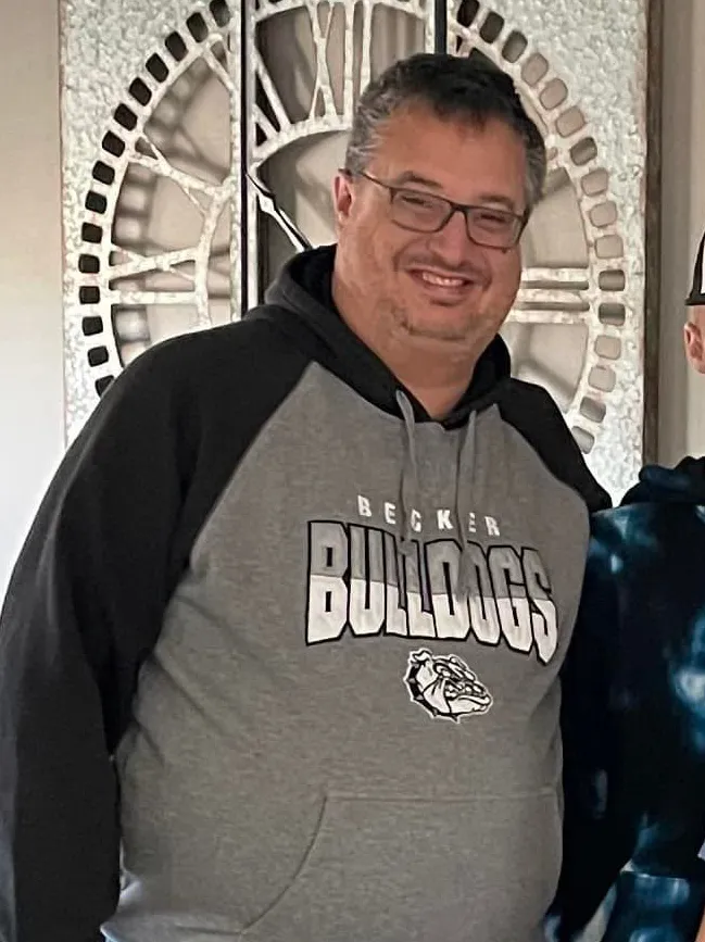 A man in a grey and black Becker Bulldogs hoodie smiles.
