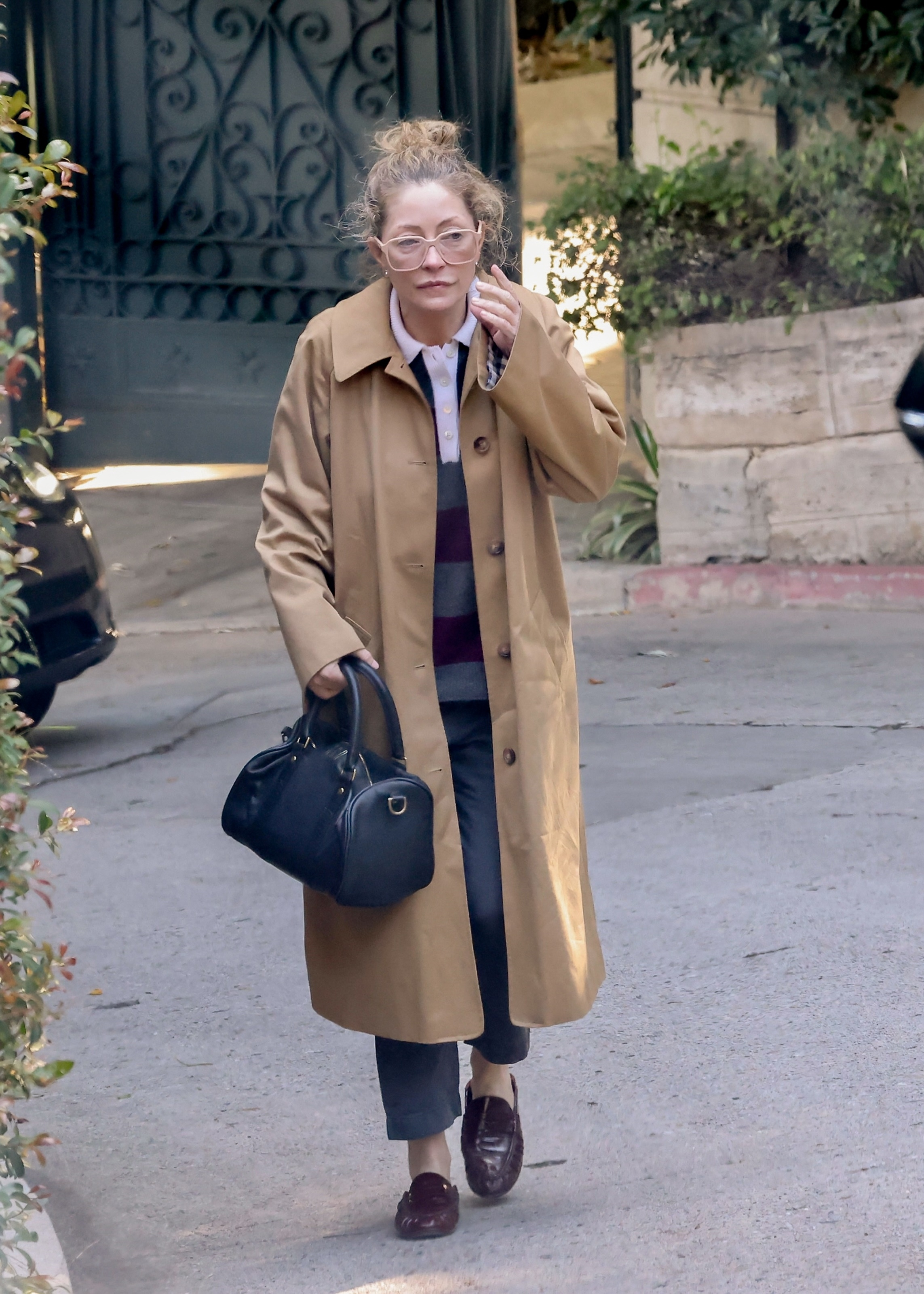 Rebecca Gayheart dressed in a long camel trench coat, carrying a black handbag, and wearing glasses while visiting Eric Dane’s West Hollywood residence.