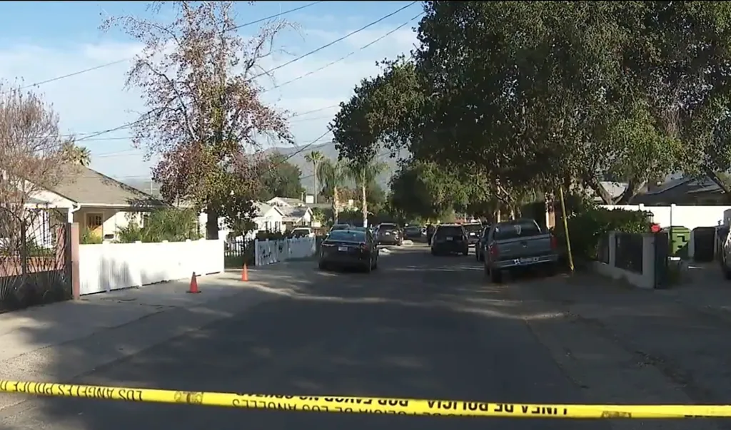 Police caution tape across a street with houses and parked cars.