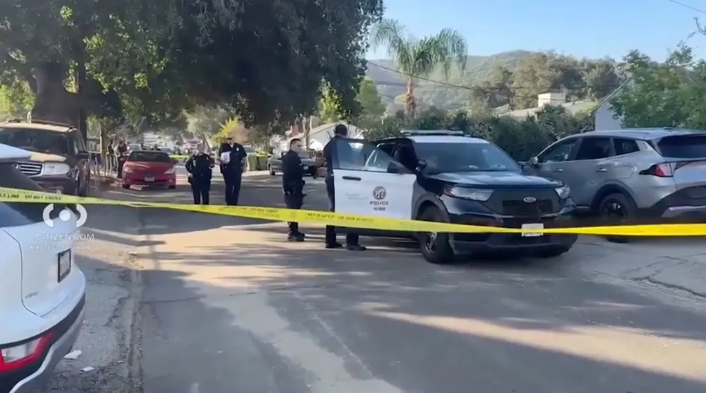 Police officers and a police vehicle behind yellow crime scene tape on a street.