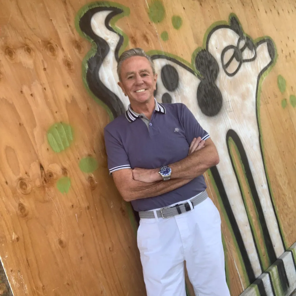 James Stephens smiling while leaning against a wooden wall with abstract graffiti.