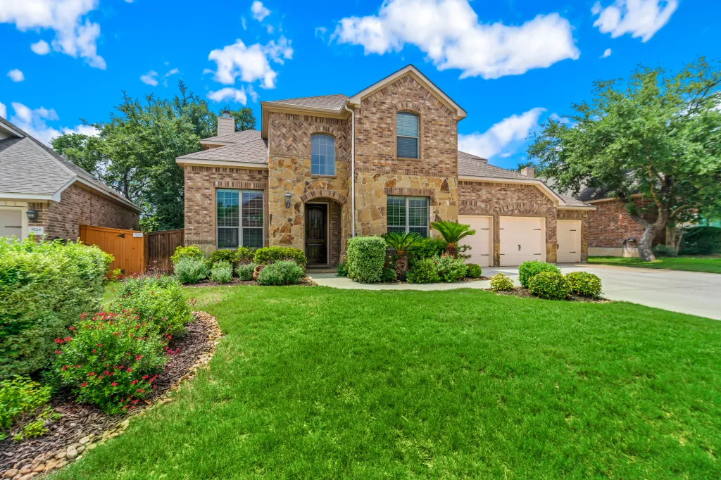 Exterior of a brick and stone house with a lush green lawn and landscaping.