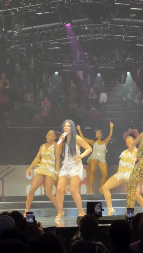 Toni Braxton performing on stage with backup dancers in sparkling dresses.