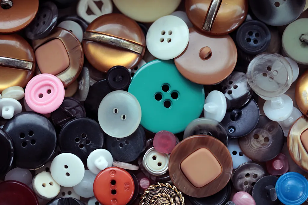 A close-up of a variety of round sewing buttons in different colors, sizes, and textures, including white, black, brown, pink, red, and teal.