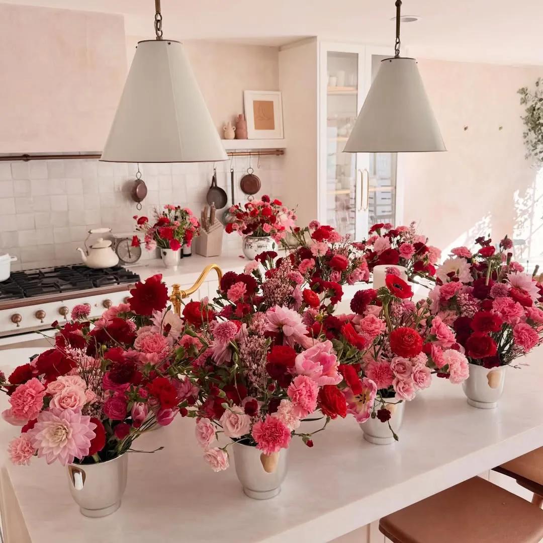 Kitchen island decorated with multiple vases of red and pink flowers.
