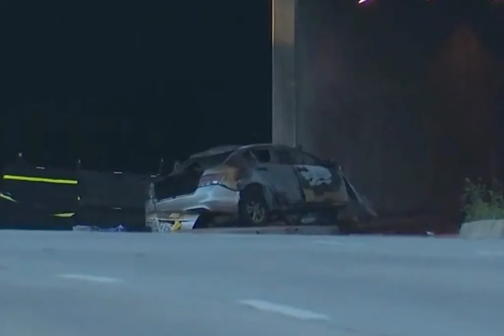A burned-out car on the side of a road at night.