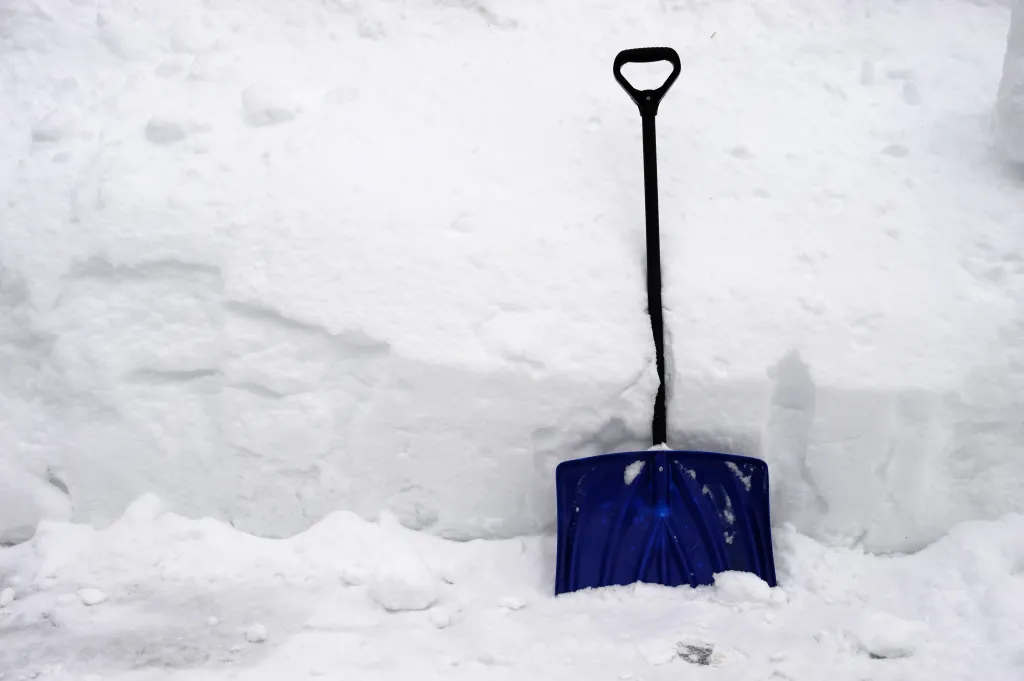 A blue snow shovel is propped against a pile of white snow.