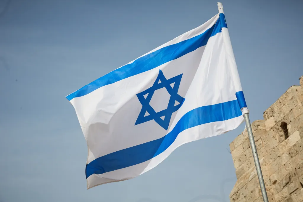 Flag of Israel against the sky and a stone wall.